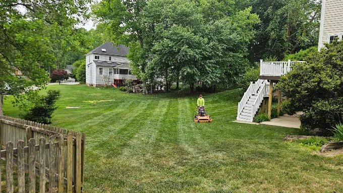 Crew member mowing a large striped backyard on a zero-turn mower
