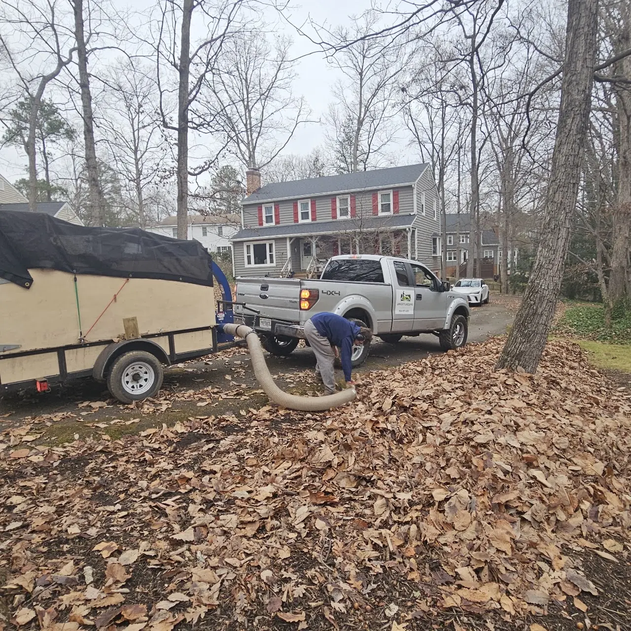 Crew vacuuming and hauling away fall leaves with truck and trailer
